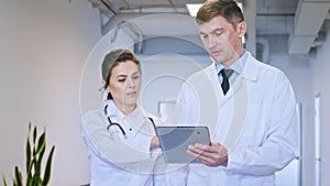 In a luminous corridor closeup to the camera the man and female doctors discussing the patient diagnostic using a