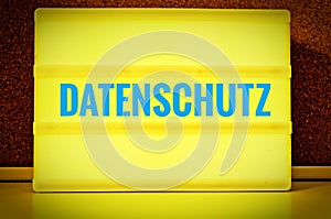 Luminous panel with the inscription in German Datenschutz in front of a pin board, in English Privacy Policy, in yellow with light