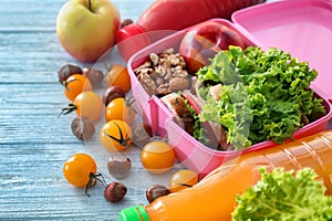 Lunch box with appetizing food and bottles of juice on light wooden table