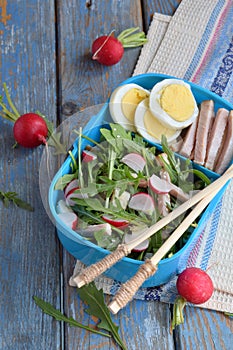 Lunch Box with salad of fresh vegetables - arugula, radish, feta cheese, ham, egg and sesame with flat bread tortilla. Healthy foo