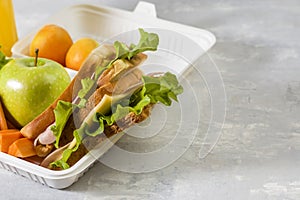 Lunch box with a sandwich, fresh vegetables and fruits, a bottle of juice on a light background. Healthy school lunch. Eco