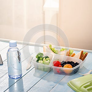 Lunch box with sandwich, vegetables, fruits and bottle of water