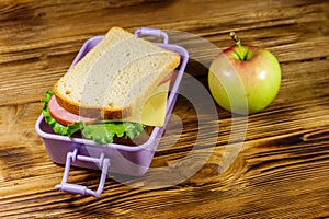 Lunch box with sandwiches and apple on wooden table