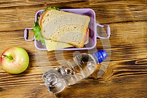 Lunch box with sandwiches, bottle of water and apple on wooden table. Top view