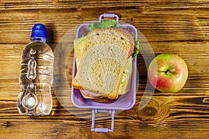 Lunch box with sandwiches, bottle of water and apple on wooden table. Top view