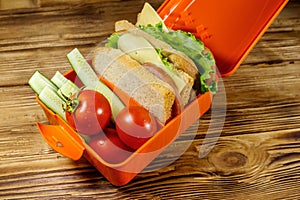 Lunch box with sandwiches and fresh vegetables on wooden table