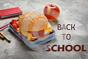 Lunch box with tasty sandwich and stationery on grey table