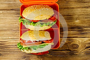 Lunch box with two homemade cheeseburgers on wooden table. Top view