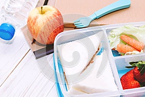 Lunch box with vegetables and slice of bread for a healthy school lunch on wooden table