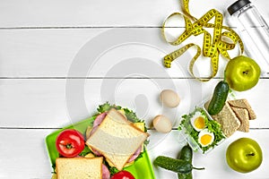 Lunch boxes with sandwiches and fresh vegetables, bottle of water and eggs on white wooden background. Top view with