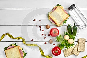 Lunch boxes with sandwiches and fresh vegetables, bottle of water, nuts and eggs on white wooden background. Top view