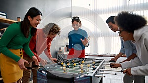 Lunch break. Group of young and happy multicultural people in casual wear playing table soccer in the modern office and