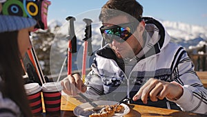 Lunch break at a ski resort. Young couple having lunch in restaurant outdoors in the mountains and communicate with each
