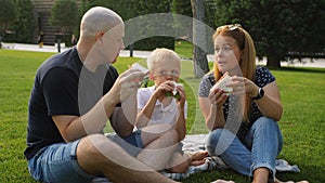 Lunch break during a walk in the park. A friendly family sat down on the grass and eat pre-prepared sandwiches with an