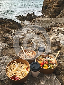 Lunch in nature. Eco bowls with pasta, vegetables and salmon on the rock against the backdrop of the ocean tide. Saint-Malo,