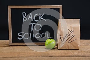 Lunch paper bag, green apple and slate with text back to school on wooden table