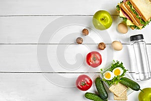 Lunch. Sandwich and fresh vegetables, bottle of water, nuts and fruits on white wooden background. Healthy eating