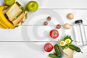 Lunch. Sandwich and fresh vegetables, bottle of water, nuts and fruits on white wooden background. Healthy eating