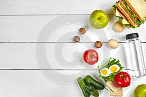 Lunch. Sandwich and fresh vegetables, bottle of water, nuts and fruits on white wooden background. Healthy eating