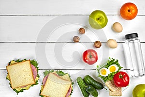 Lunch. Sandwich and fresh vegetables, bottle of water, nuts and fruits on white wooden background. Healthy eating