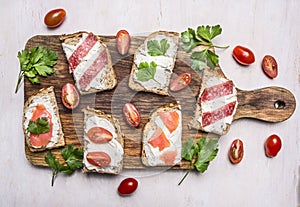 Lunch with sandwiches with salami and smoked red fish with parsley leaves and curd cheese wooden rustic background top view clo