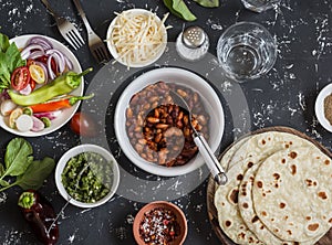 Lunch table - tortilla, stewed beans, vegetables, cheese, spicy green chile sauce. Delicious, vegetarian food. On a dark