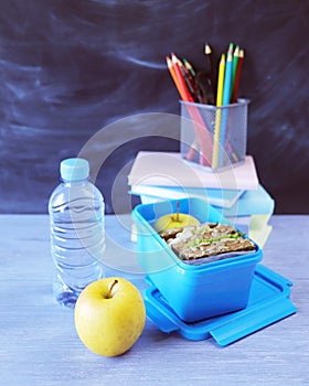 Lunchbox with sandwich, water bottle, apple, books and stationery on wooden table