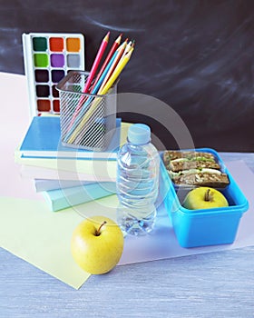 Lunchbox with sandwich, water bottle, apple, books and stationery on wooden table