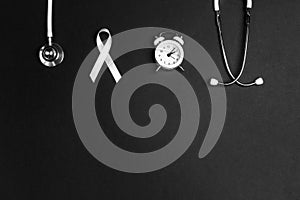 Lung cancer awareness background with white ribbon, alarm clock and stethoscope on black