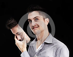 Lurking insanity. Young man lifting a mask off his face and revealing a deranged expression.