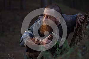 Lurking medieval red-haired viking warrior with beard with an ax in forest