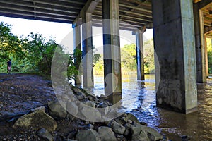 The lush brown waters flowing underneath a freeway underpass with tall concreate pillars at the Chattahoochee River