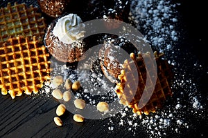Lush fresh chocolate muffins sprinkled with powdered sugar, lay against the dark wood. Round Belgian waffles. Also have