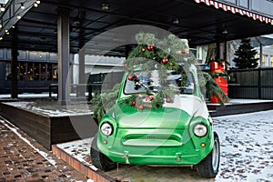 Lush green spruce on the roof of a green, old retro car. Pine decorated with red Christmas balls and garlands. Christmas tree on i
