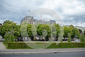 Lush green trees in the garden in front of the medieval style hotel on cloudy sky background