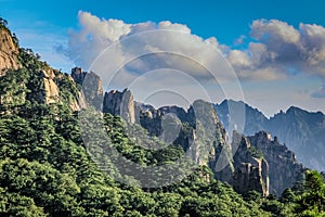 Lush green trees and sharp rocks slope from the top right down to the lower right corner in Huang Shan