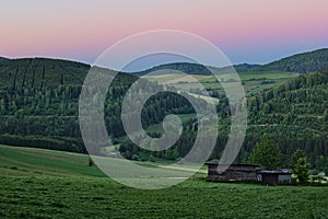 Lush green valley with fertile fields and forest under a pink evening sky at dusk