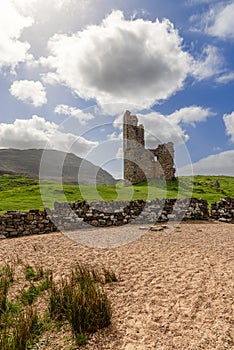 Lush landscape with Ardvreck Castle remains, framed by expansive sky and ancient stone boundary