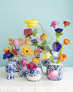 Lush natural light stillife with old Dutch Delft blue lidded vase with multicolored flowers on white linen against a blue