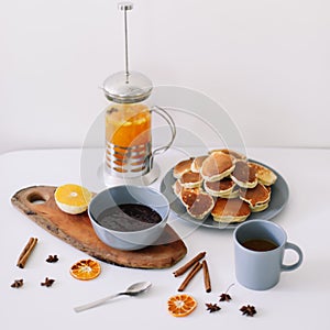 Lush pancakes and teapot with spices, cup of tea with orange, cinnamon, anise. Tasty breakfast on white background. Good morning