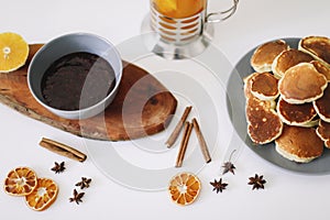 Lush pancakes and teapot with spices, cup of tea with orange, cinnamon, anise. Tasty breakfast on white background. Good morning