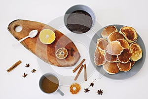 Lush pancakes and teapot with spices, cup of tea with orange, cinnamon, anise. Tasty breakfast on white background. Good morning