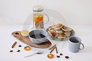 Lush pancakes and teapot with spices, cup of tea with orange, cinnamon, anise. Tasty breakfast on white background. Good morning