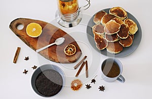 Lush pancakes and teapot with spices, cup of tea with orange, cinnamon, anise. Tasty breakfast on white background. Good morning