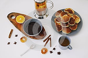 Lush pancakes and teapot with spices, cup of tea with orange, cinnamon, anise. Tasty breakfast on white background. Good morning