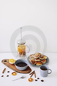 Lush pancakes and teapot with spices, cup of tea with orange, cinnamon, anise. Tasty breakfast on white background. Good morning