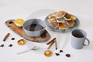 Lush pancakes and teapot with spices, cup of tea with orange, cinnamon, anise. Tasty breakfast on white background. Good morning