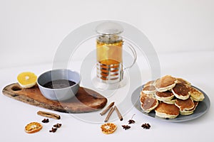 Lush pancakes and teapot with spices, cup of tea with orange, cinnamon, anise. Tasty breakfast on white background. Good morning