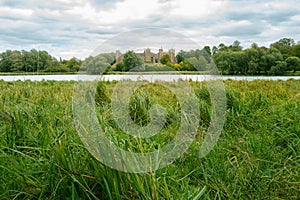 Lush vegetation seen in front of a medieval lake and beyond a famous English castle in the east of England.