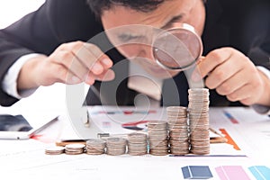 Lustful businessman with a magnifying glass in hand carefully observes a row of dollar coins